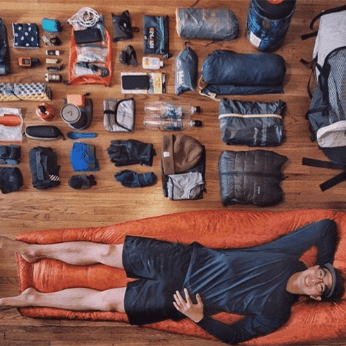 Man laying on sleeping bag next to camping gear