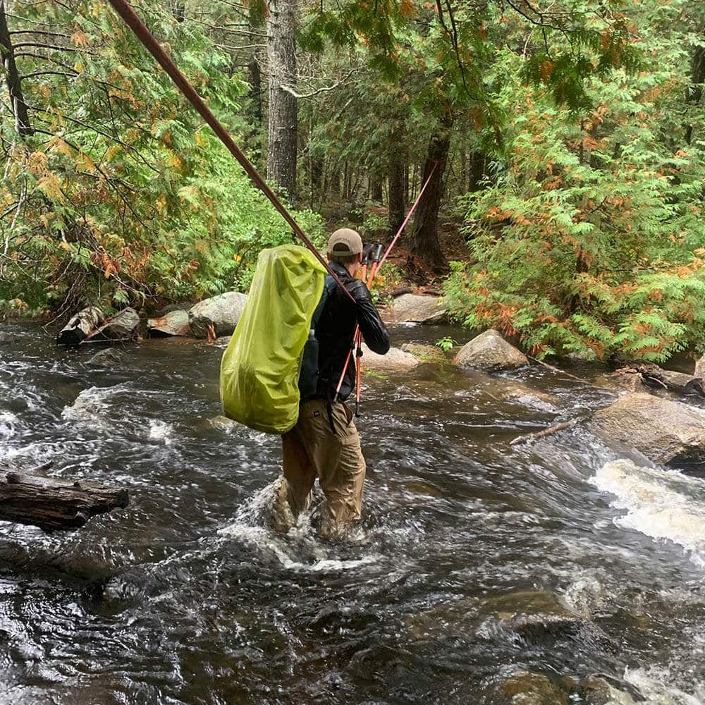Person crossing rushing creek while holding rope