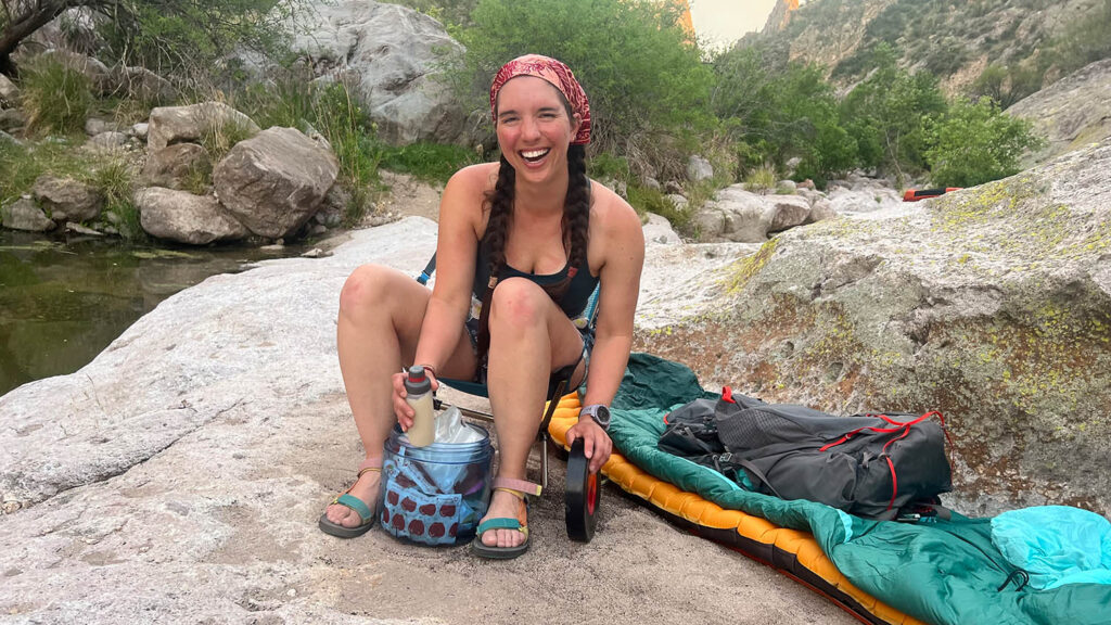 Woman smiling sitting on ground opening bear canister