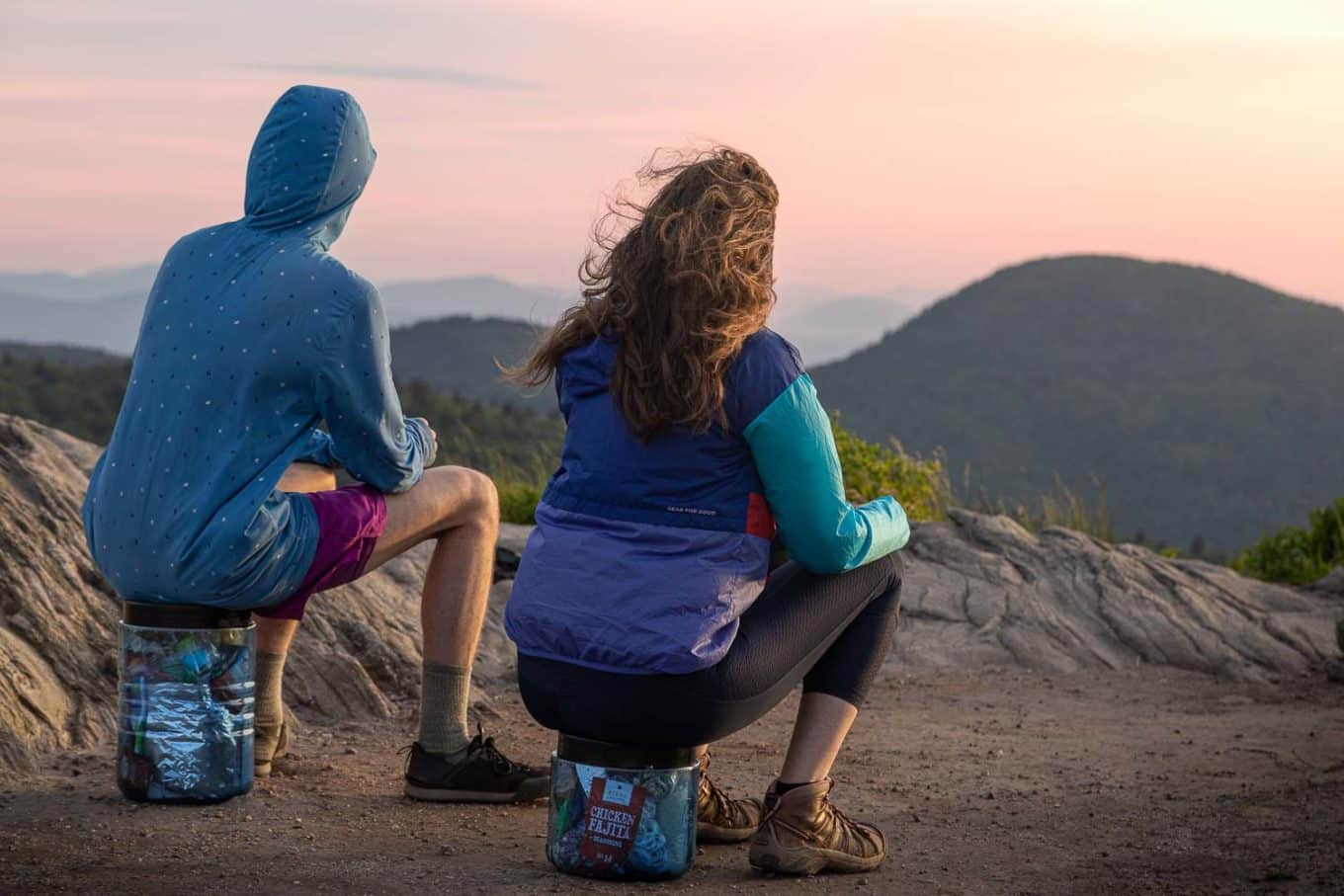 Two people sitting on BearVault bear canisters looking at sunset