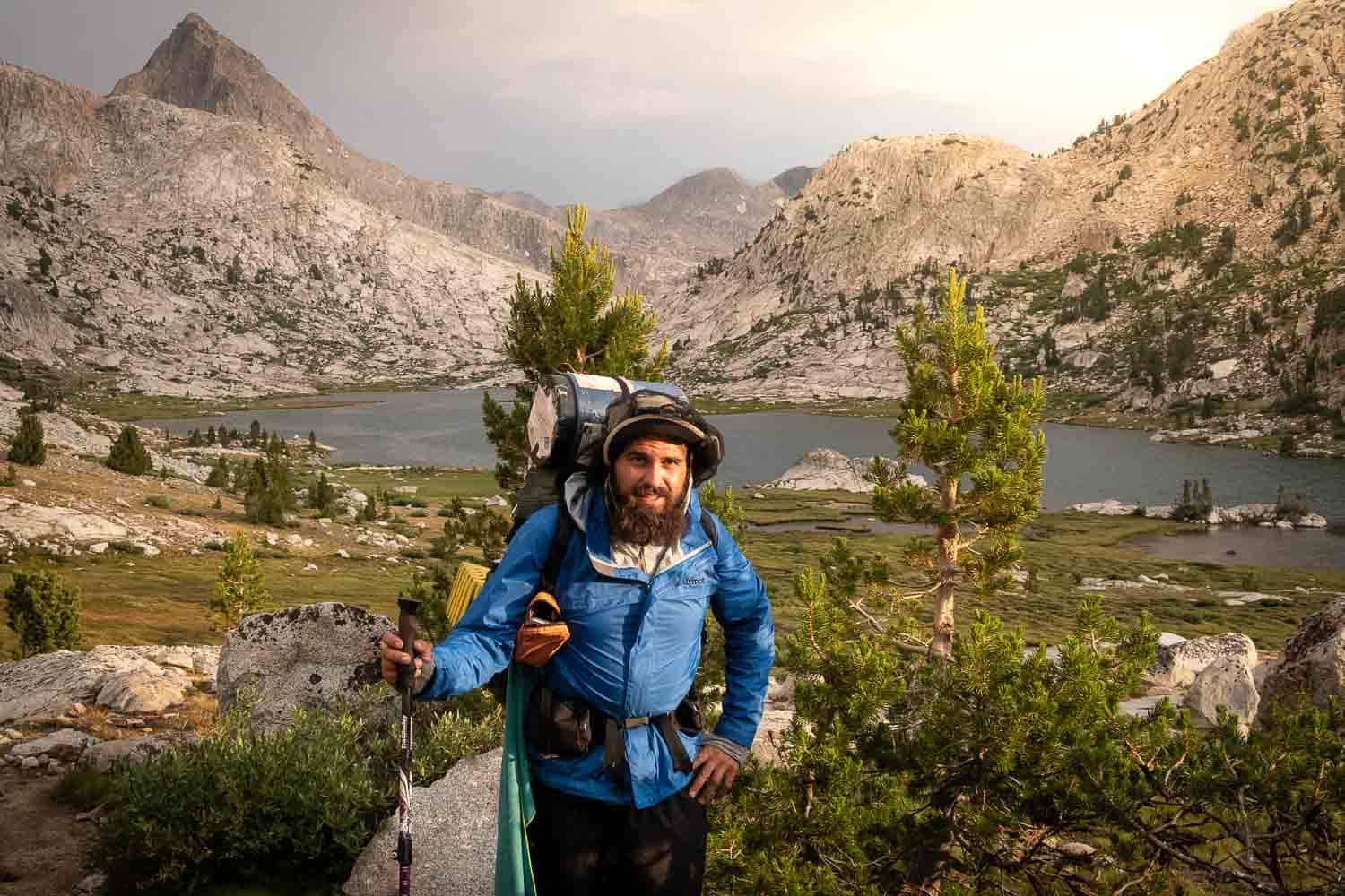 Man in front of mountain lake with BearVault bear canister strapped to the top of his pack