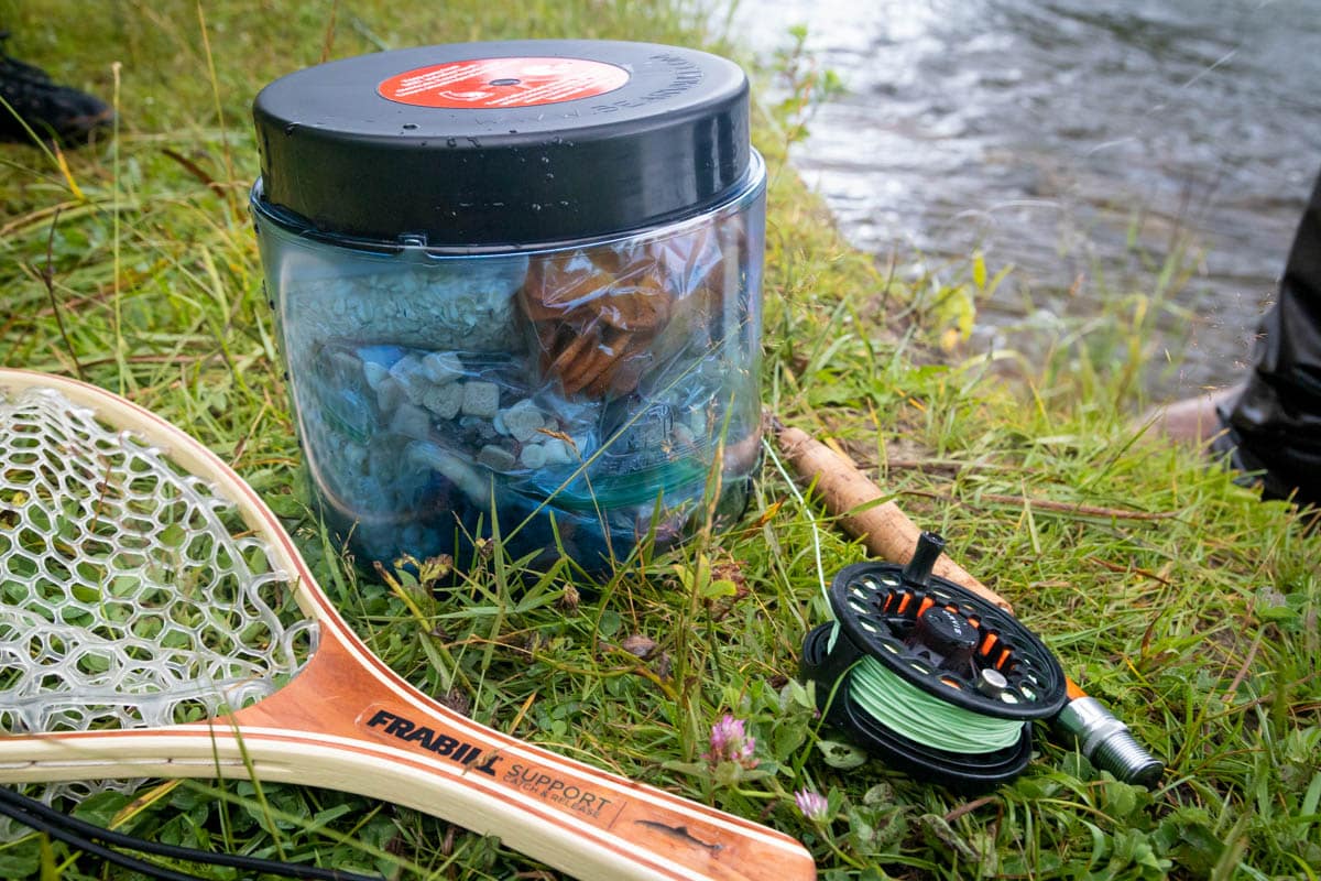 A bear canister sitting between a fly fishing net and a rod