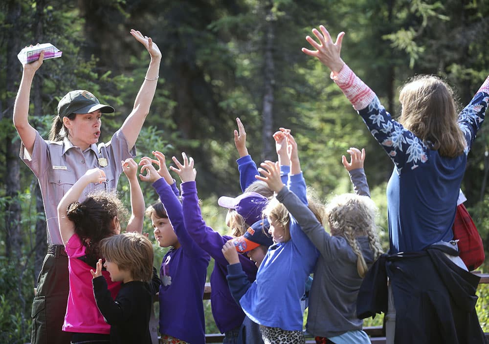 A park ranger instructs a group of children how to stand tall and say "hey Bear"