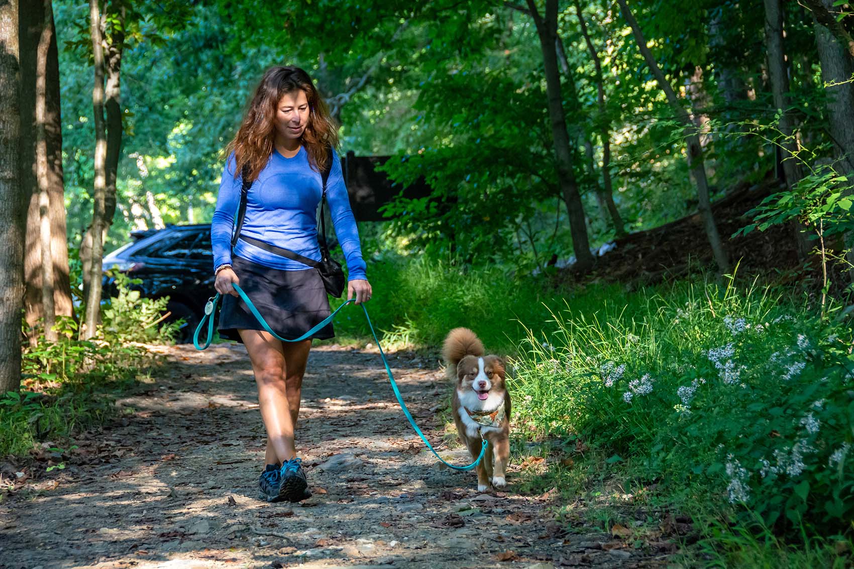 A woman walks her dog down a wide path on a leash demonstrating proper dog and bear encounter technique