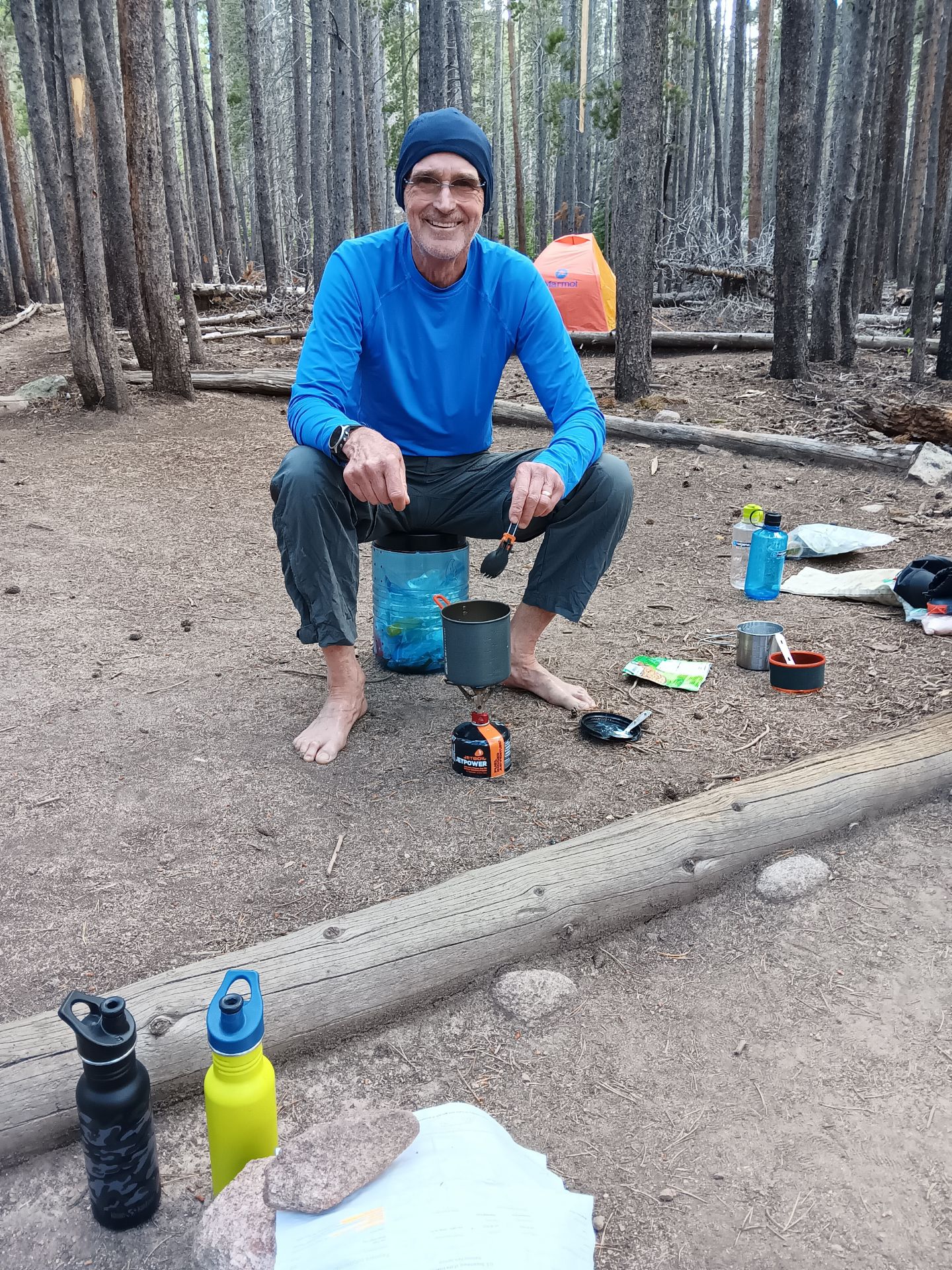 Hiker sits on bear canister and prepares a meal in Rocky Mountain National Park.