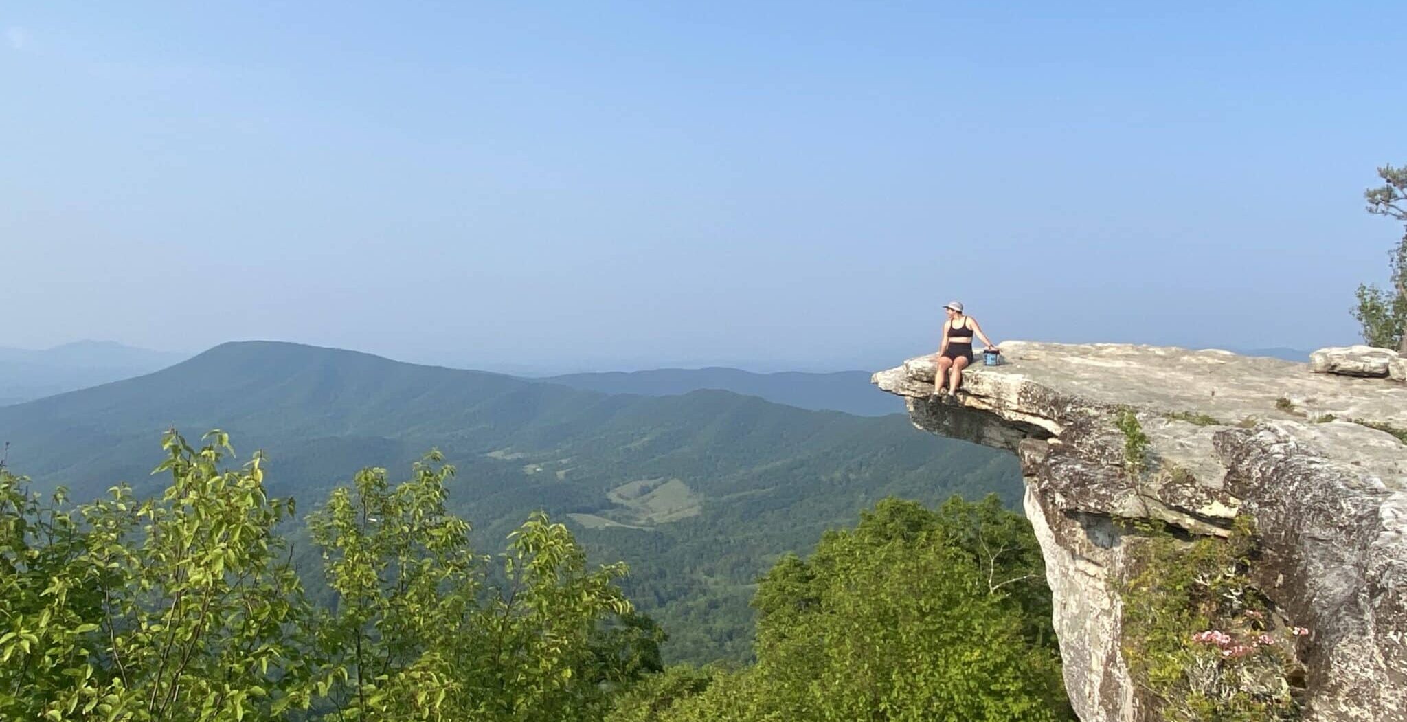 A thru-hiker relaxes on a cliff edge along the Appalachian Trail.