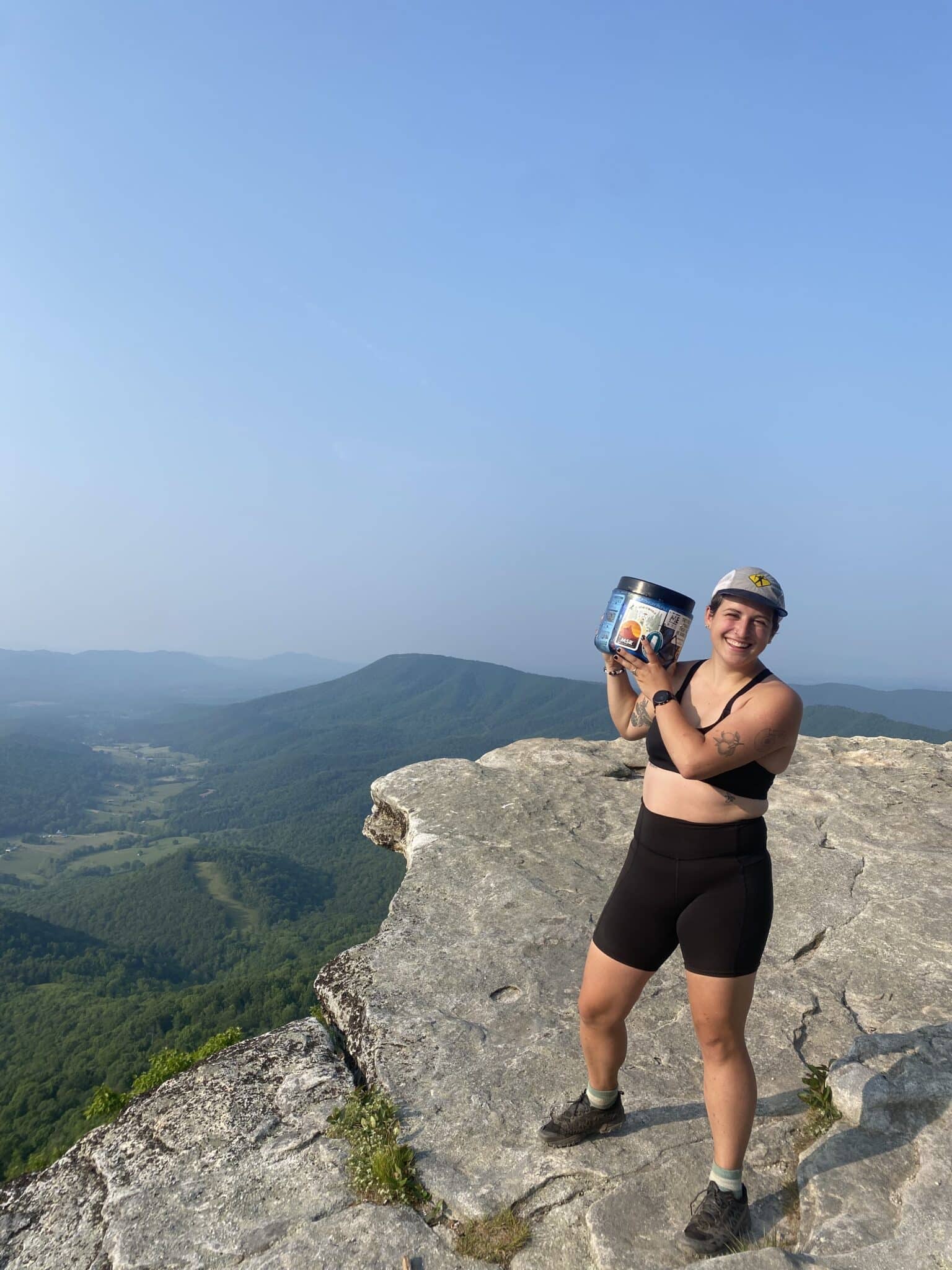 An Appalachian Trail Thru-hiker lifts a bear canister at a viewpoint.