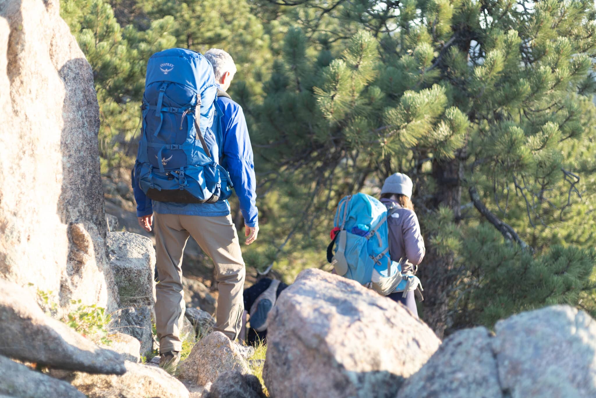 Two backpackers walk through rocks and into the woods